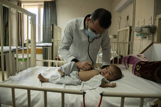 戴口罩的男医生检查躺在医院病床上的幼童